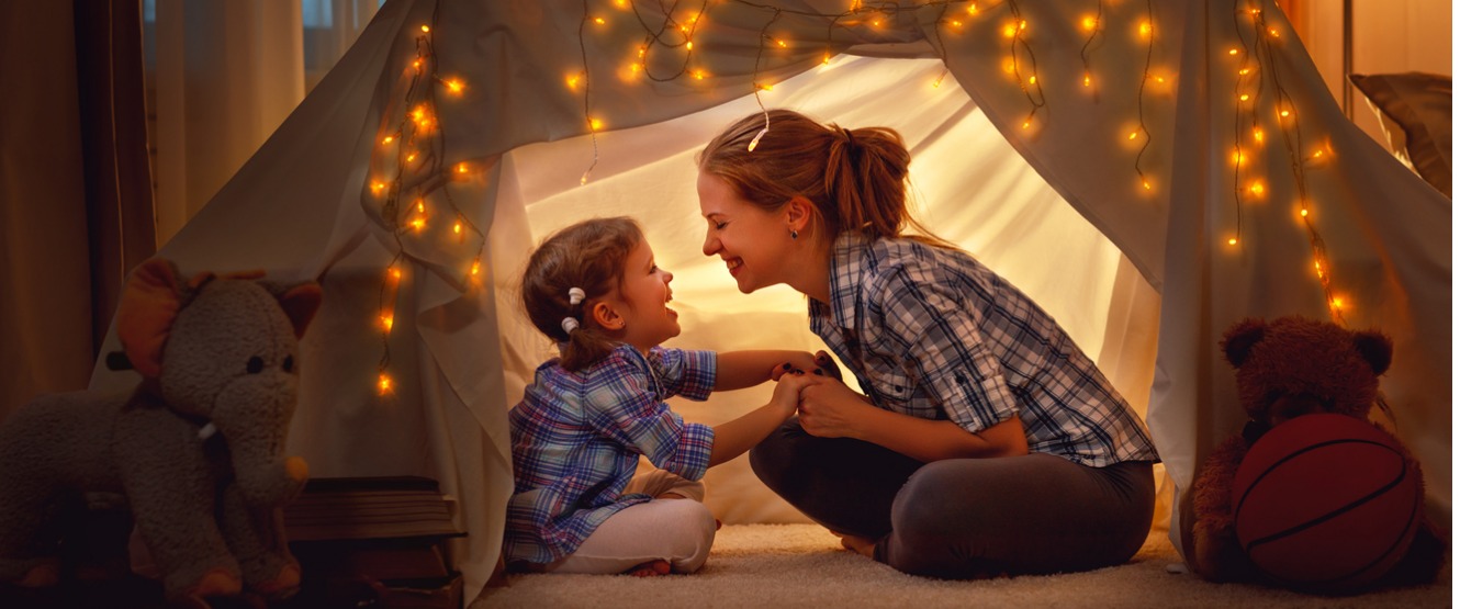 Happy mother and daughter playing in tent at home